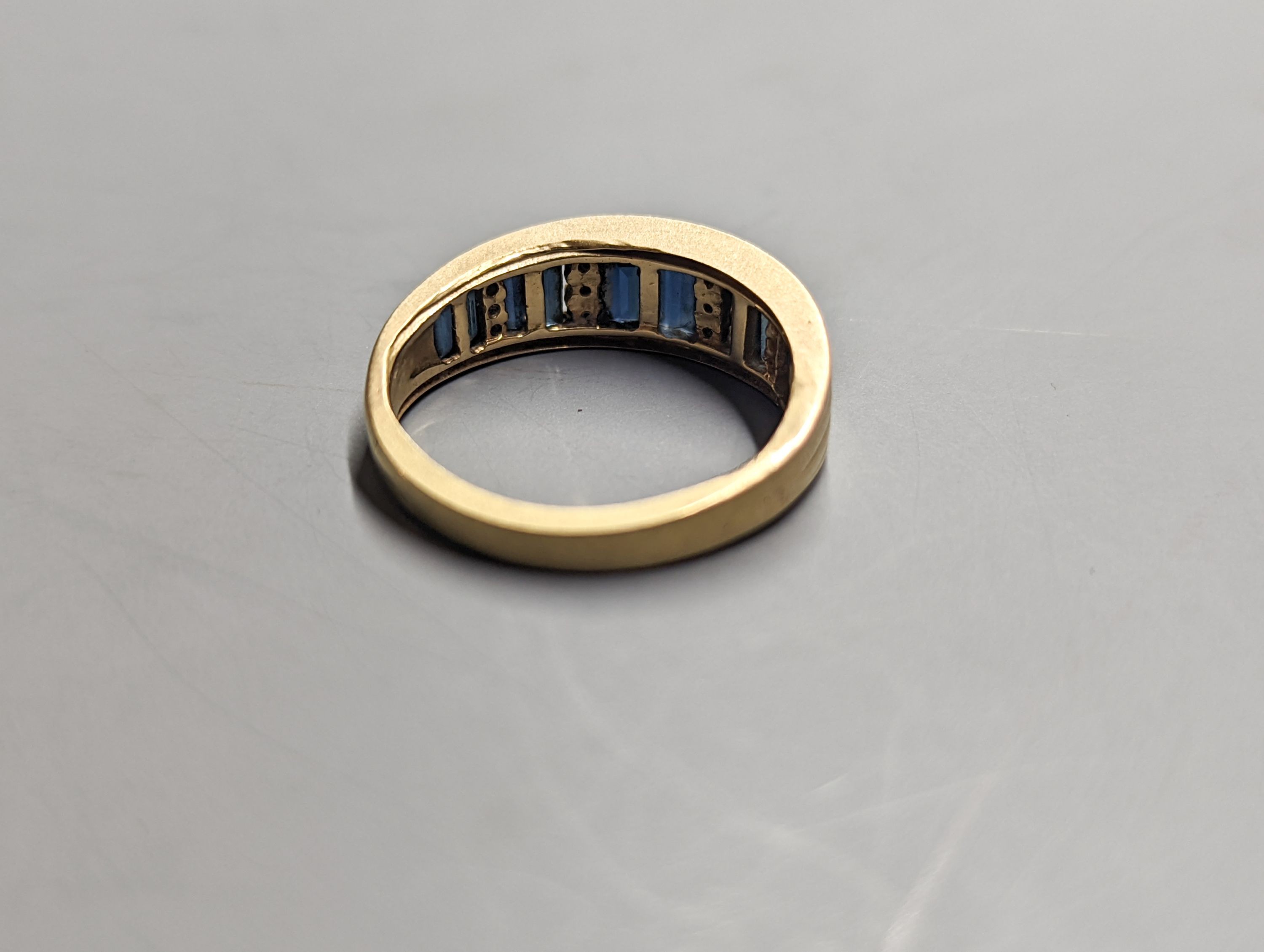A modern yellow metal, diamond chip and graduated baguette cut sapphire set half hoop ring. size O, gross weight 4.2 grams.